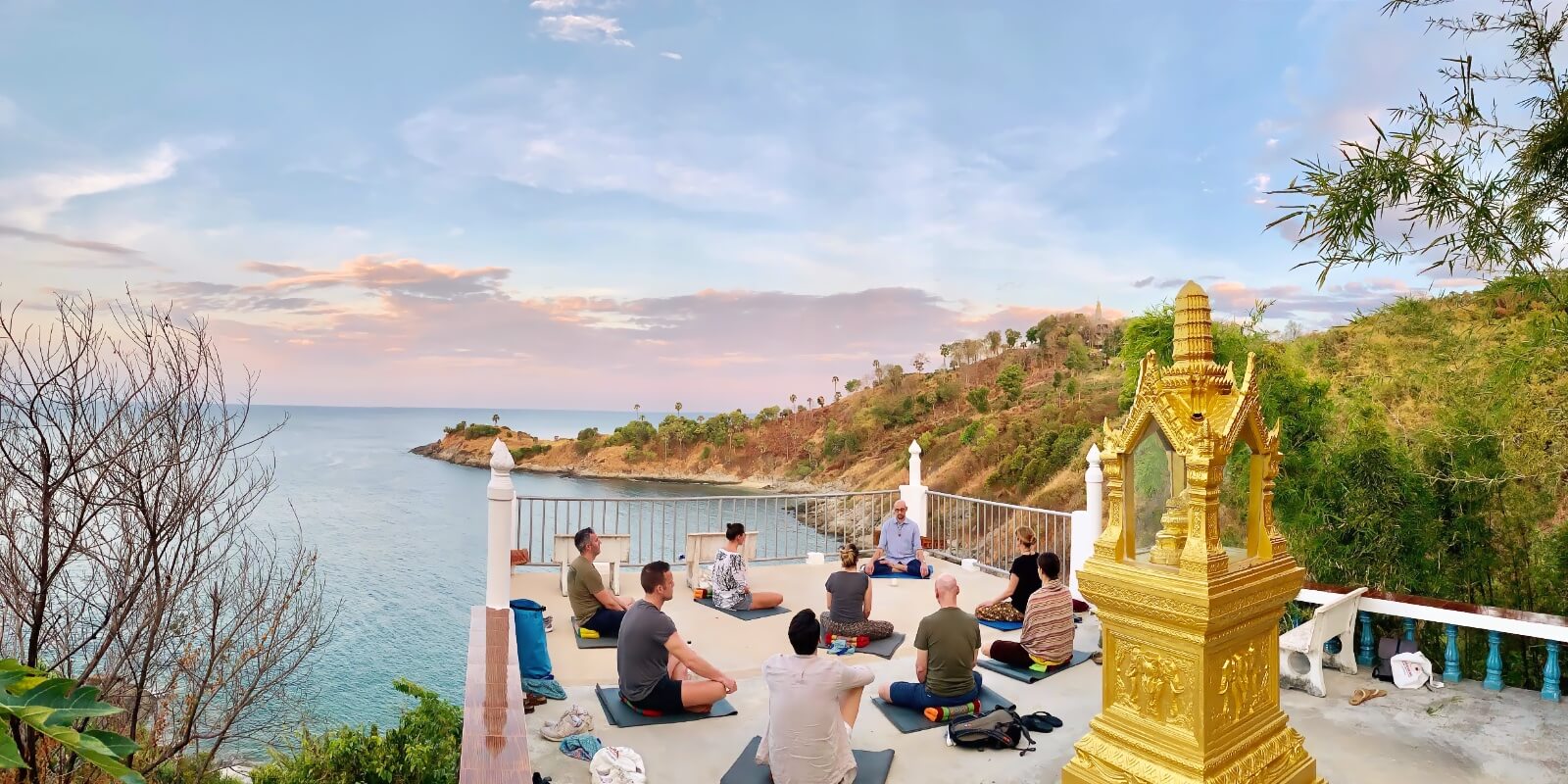 Nine people meditate together on a platform above the ocean, at Promthep Cape in Phuket during a meditation retreat.