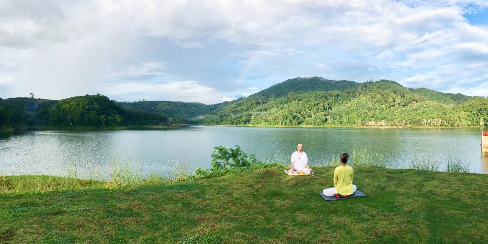 Tobi Warzinek provides personal guidance to a woman. They meditate together in nature at a lake.