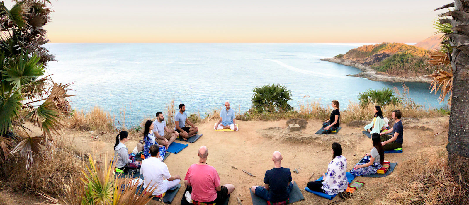 Phuket Meditation Retreat with a large group of people meditating together atop Promthep Cape, above the Andaman sea.