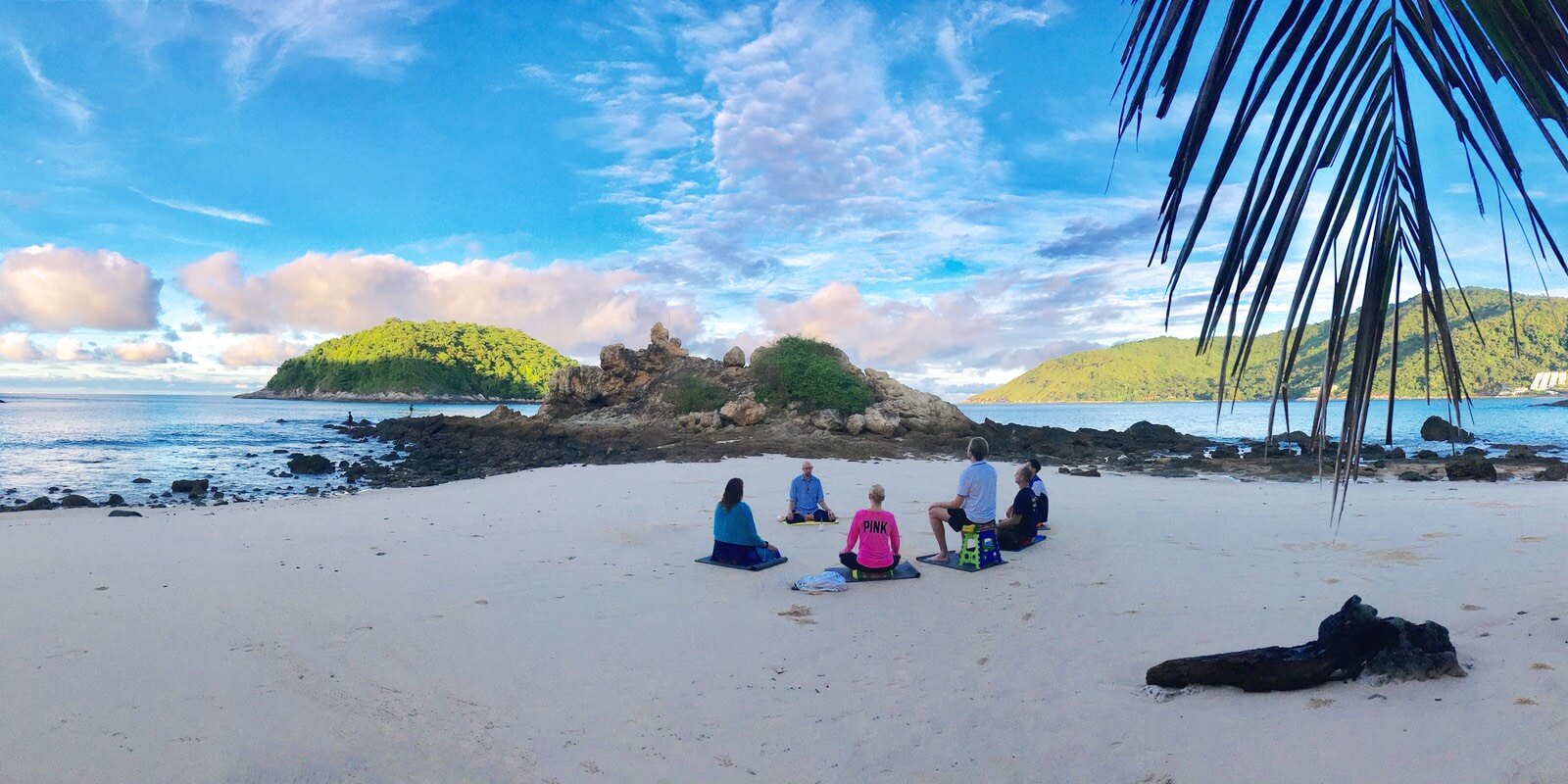 Six people meditate together at Yanui beach in Phuket during a meditation retreat.