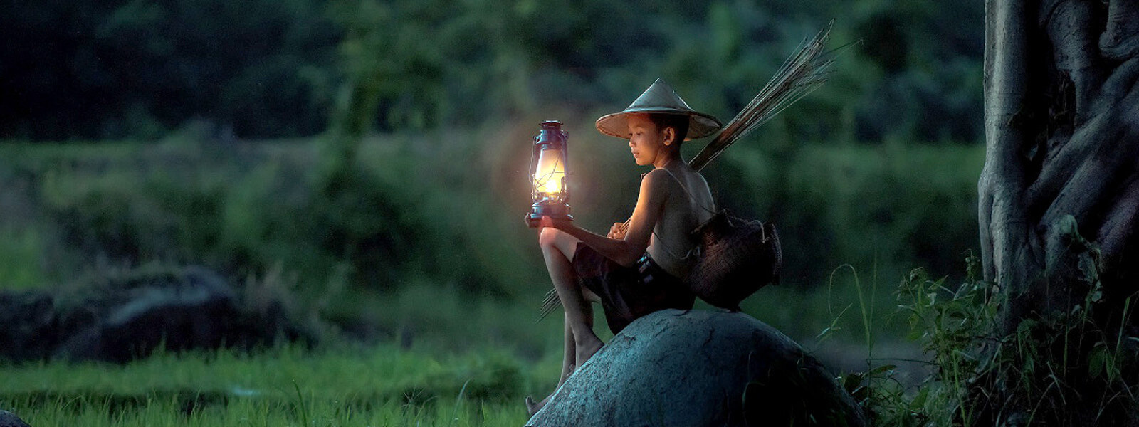 Thai boy sits on a rock, holding an oil lamp.