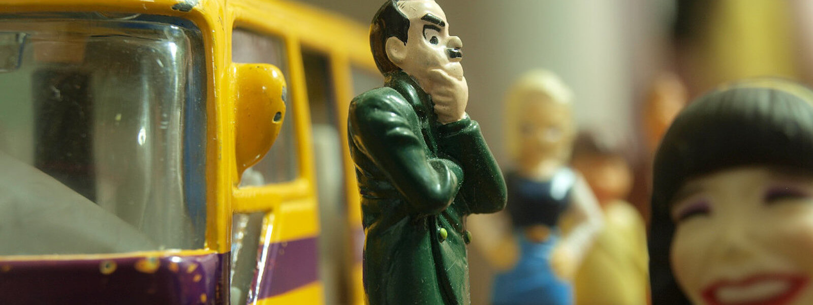 A tiny figurine of a man standing in front of a yellow bus, apparently worrying about something.