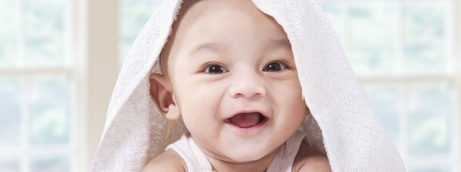 Little baby with towel on its head laughing into the camera.