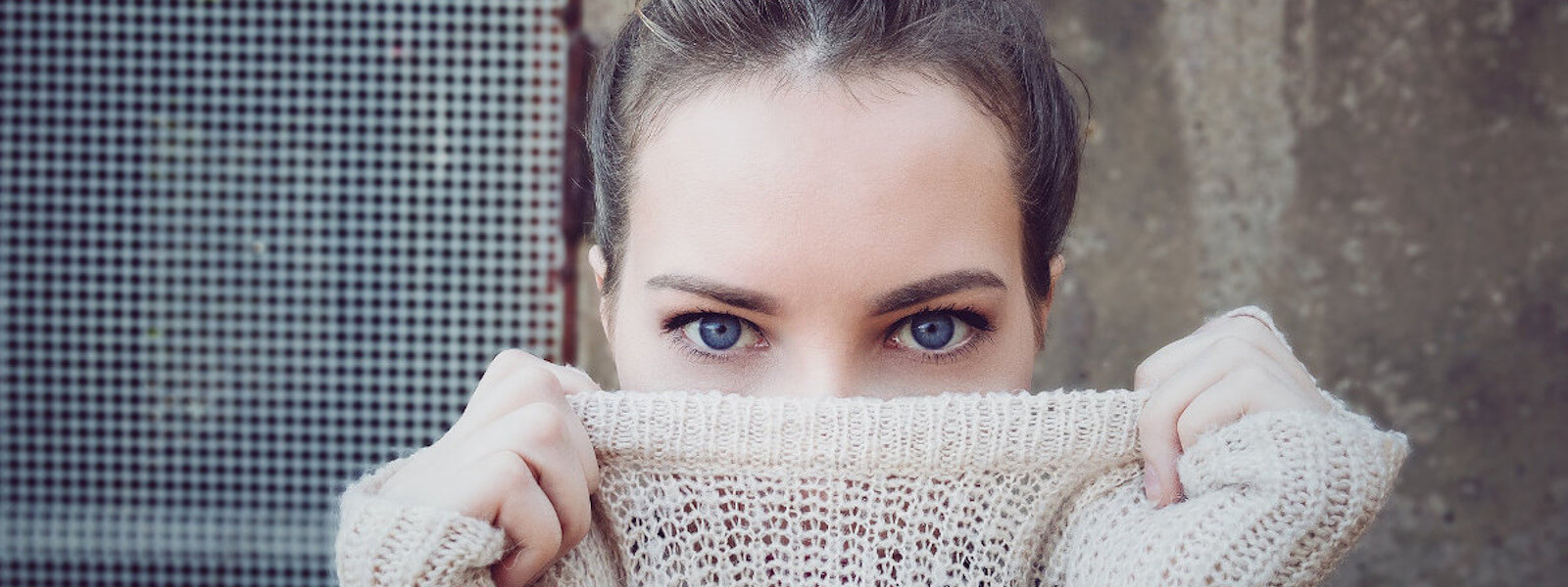Young woman hiding part of her face behind a white turtleneck sweater.