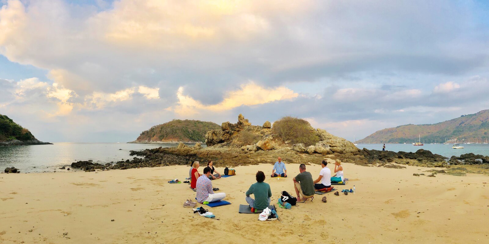 Nine people meditate together in a circle on Yanui beach in Phuket during a retreat.