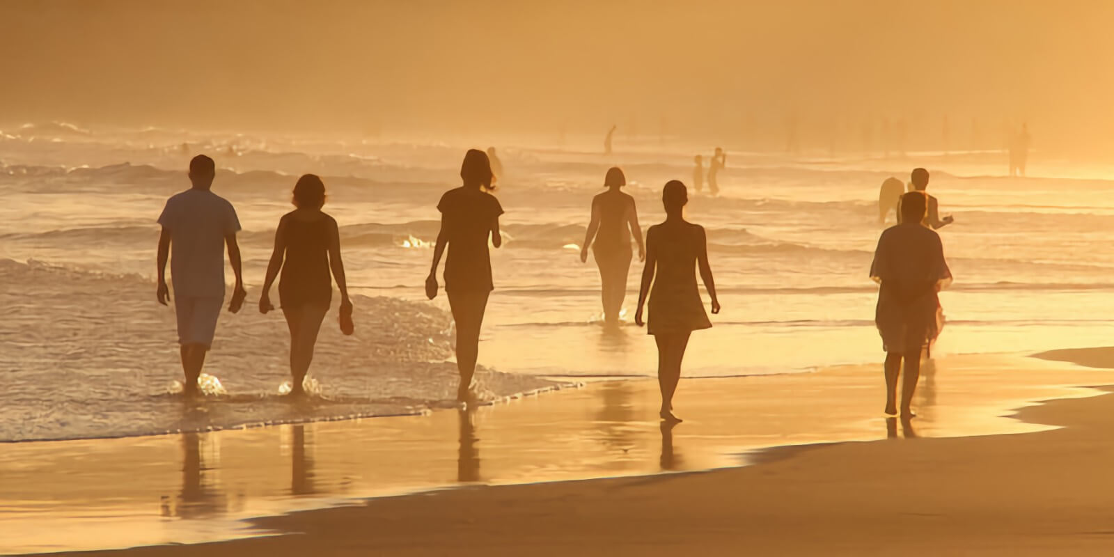A group of people walk at a misty beach together during sunset.