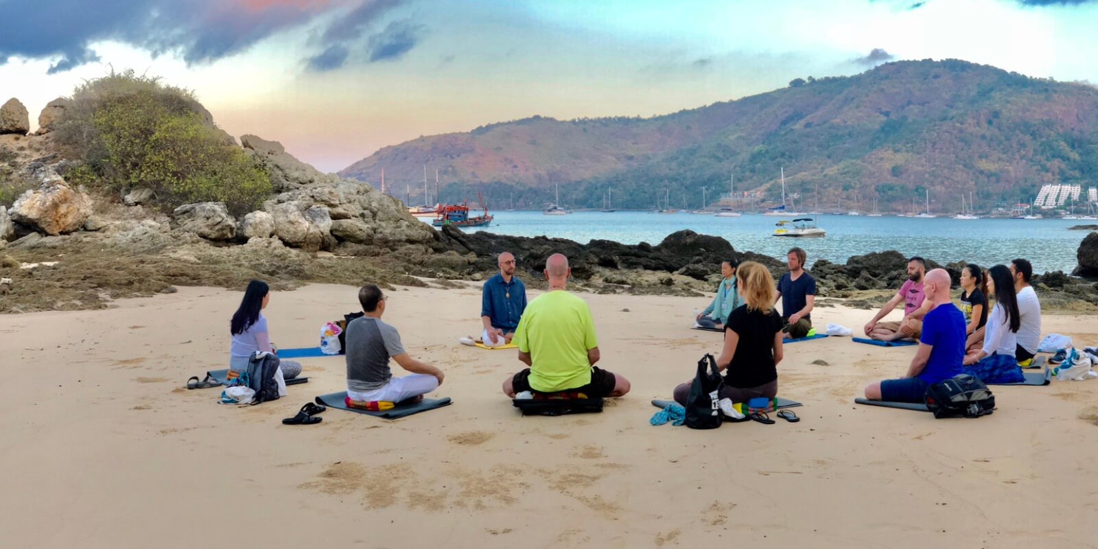Twelve people sit in a circle and meditate at Yanui Beach in Phuket during a retreat.