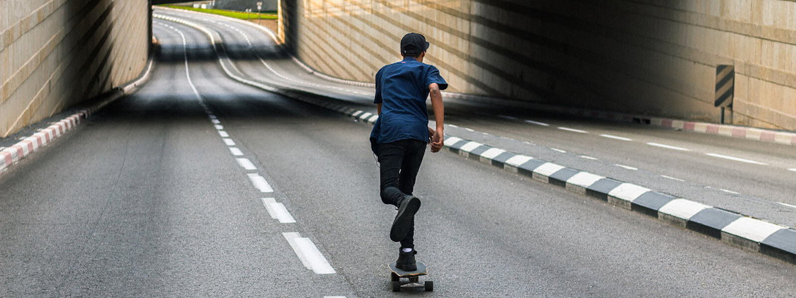 A male longboard skater is skating down an empty street in a city below bridges.