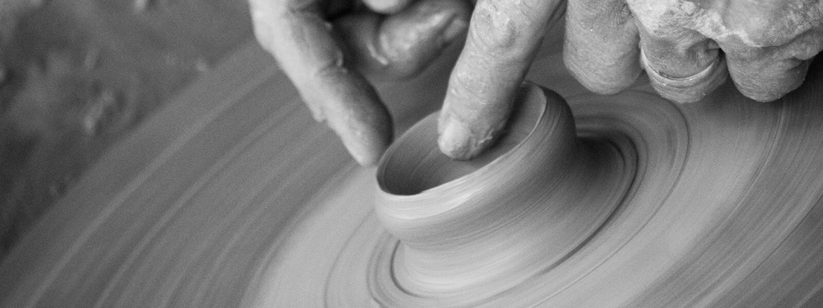 Two hands shaping a piece of clay on a potter's lathe.