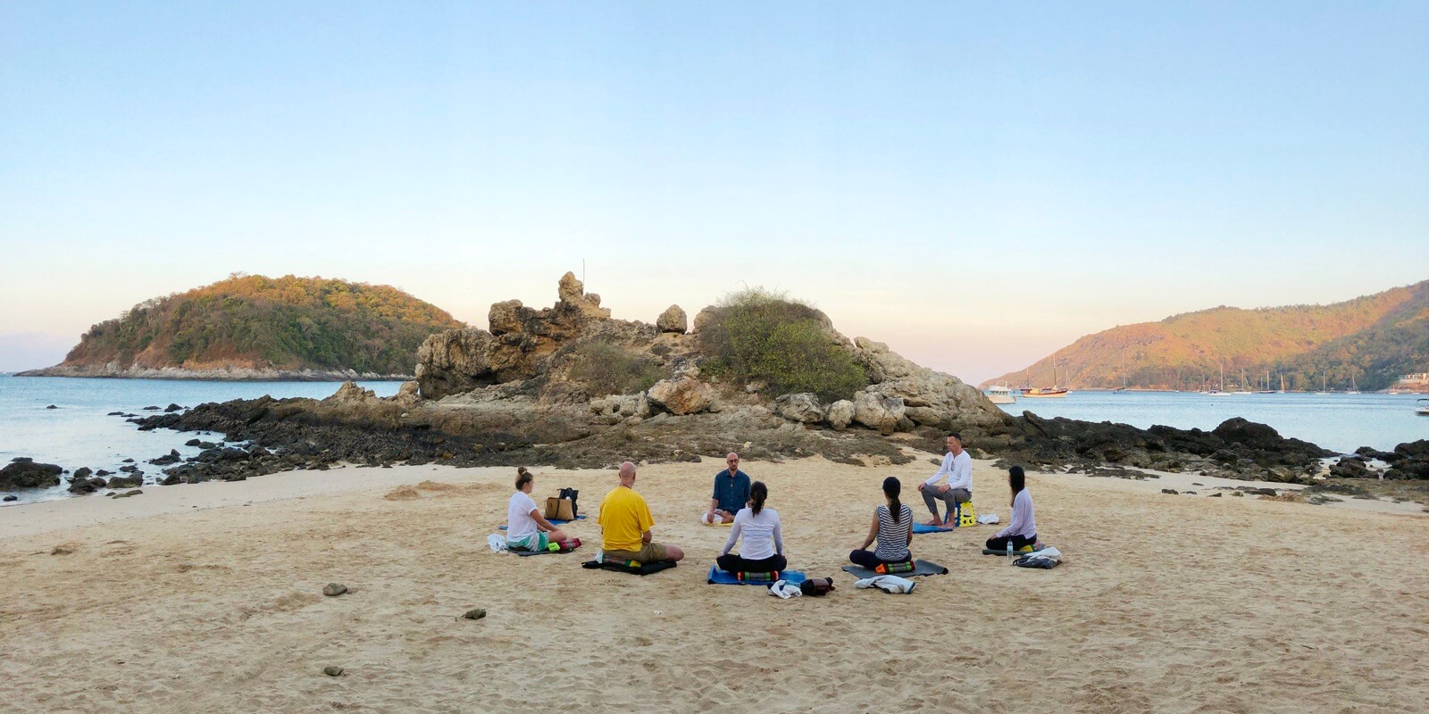 Seven people meditate together in a group at Yanui Beach in Phuket.