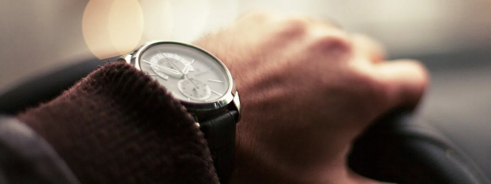A male hand with a watch is holding the steering wheel of a car.