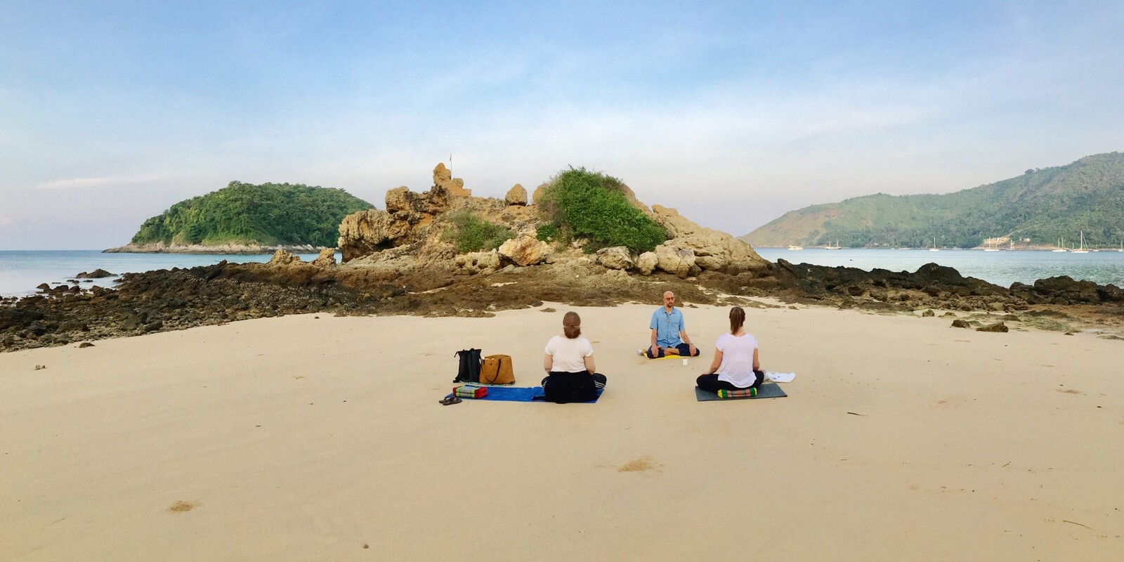Three people meditate at Yanui beach together during the morning hours in Phuket.