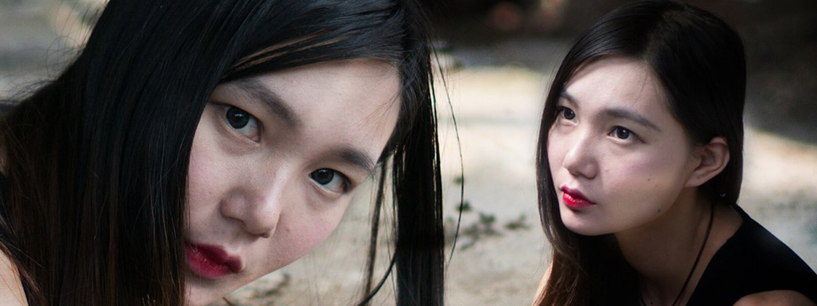 Two identical asian women are looking at the camera and each other.