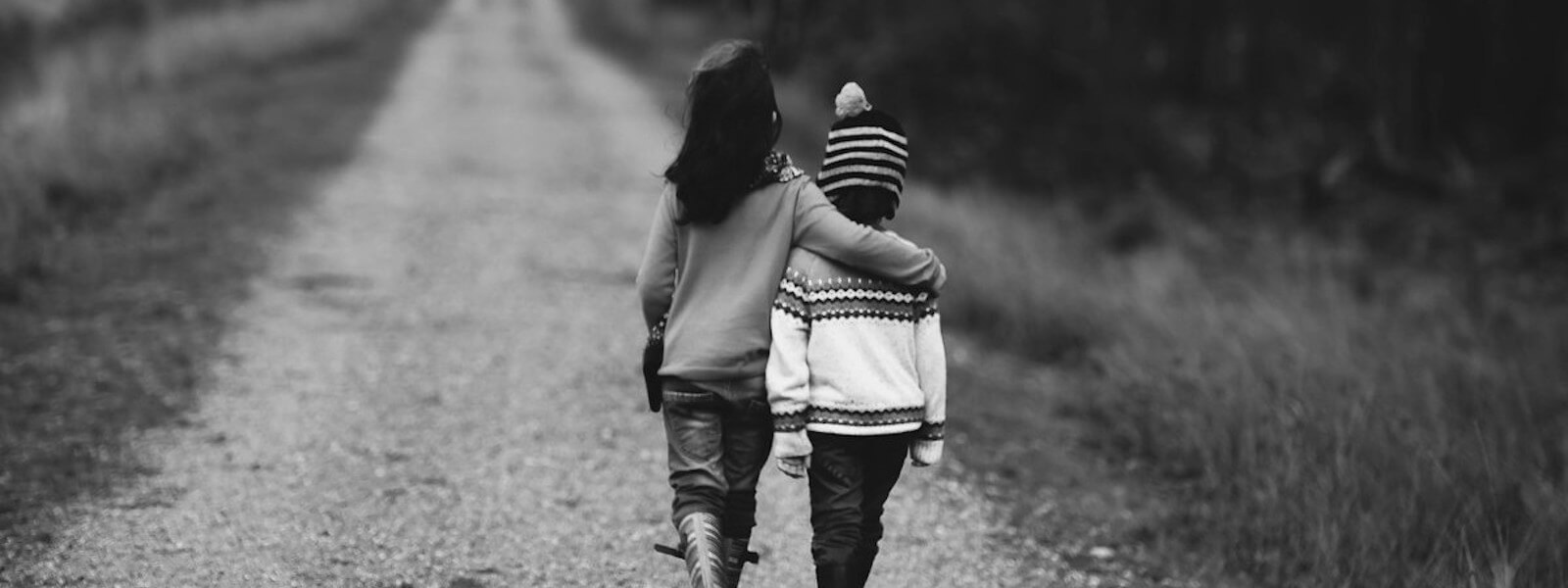 A boy and a girl walk arm in arm together on a dirtroad.