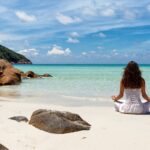 Phuket Meditation Retreats - woman in white dress meditates at a beach