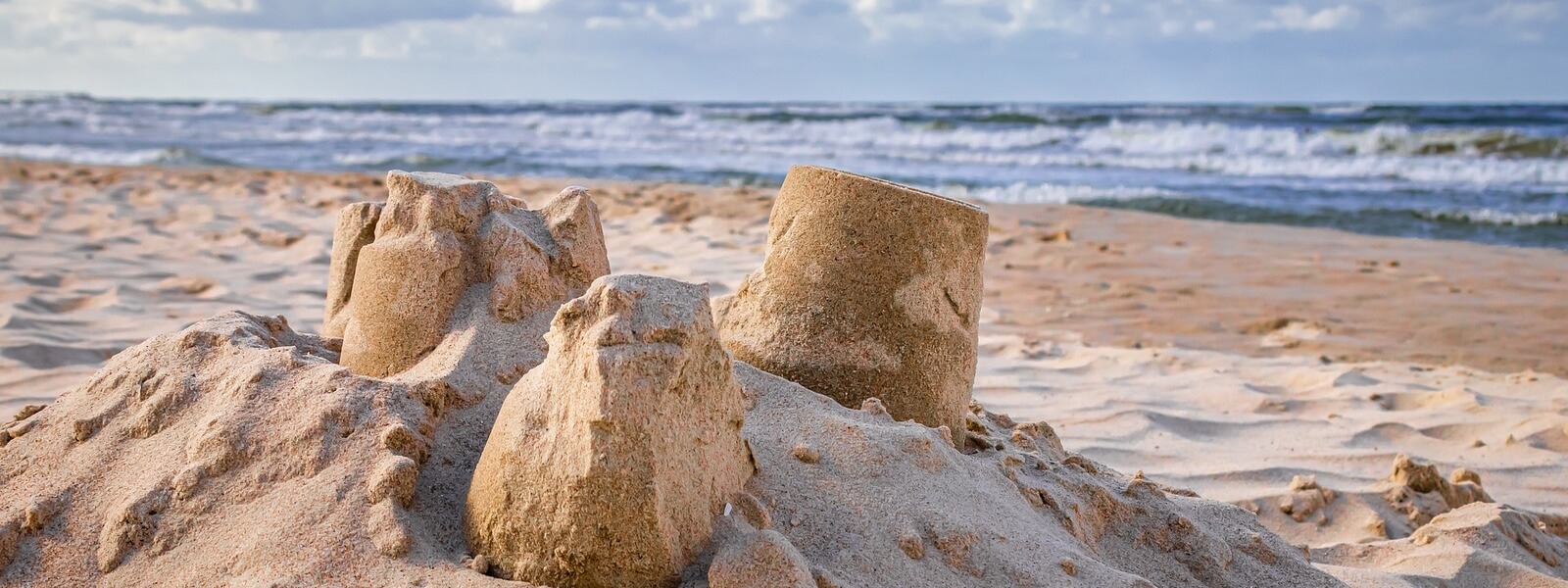 Sandcastles on a beach, eroding in the wind. The sea is in the background.